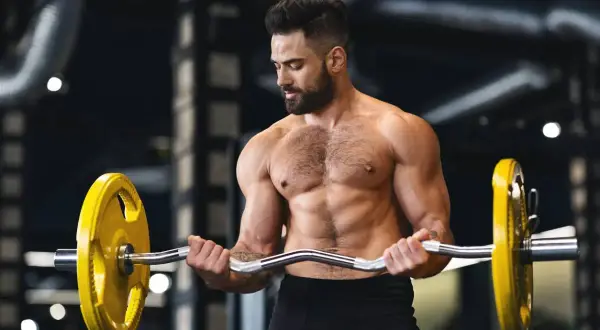 Un homme musclé s'entraîne avec une barre chargée de poids jaunes, concentré sur sa prise de masse.
