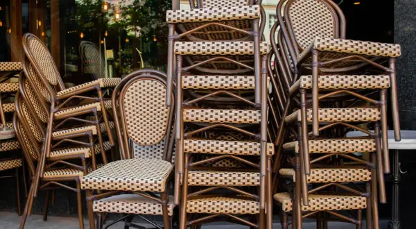 Gestapelte braune Bistrostühle mit geflochtenen Sitzflächen und Rückenlehnen vor einem Restaurant.