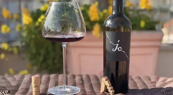 Un calice di vino rosso e una bottiglia di Negroamaro Puglia, con tappo e cavatappi, su un tavolo all'aperto.