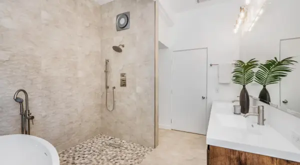 Une salle de bain moderne avec une baignoire îlot, une douche à l'italienne aux galets et un double lavabo. Un exemple de les plus belles douches à l'italienne.
