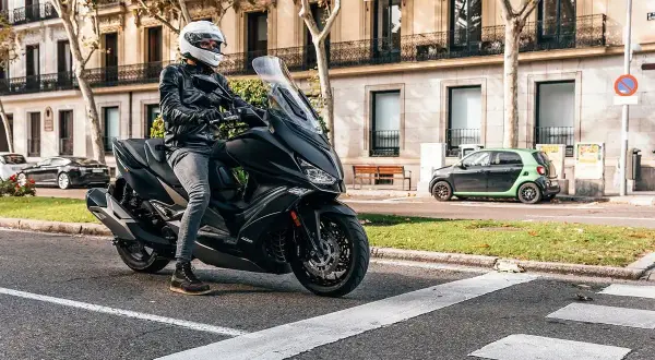 Conductor con casco blanco en un scooter negro, listo para rodar. Una imagen que evoca las mejores marcas de motos y la libertad en la ciudad.
