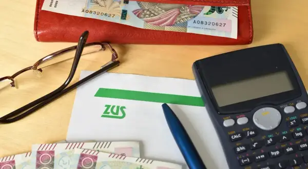 Na stole leżą dokumenty ZUS, pieniądze, kalkulator i okulary. Przygotowanie do złożenia wniosku o świadczenie wspierające.