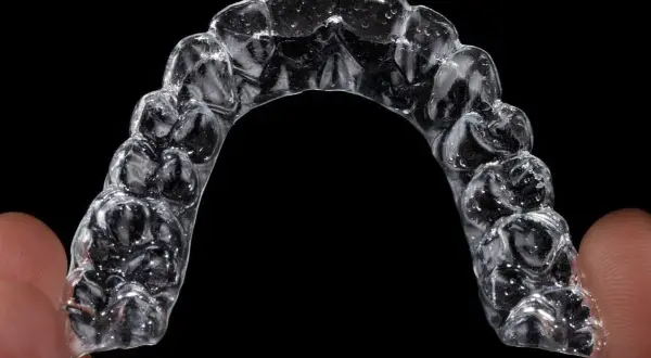 Przezroczysty aparat Invisalign, trzymany palcami, z widocznymi indywidualnymi nakładkami na zęby.