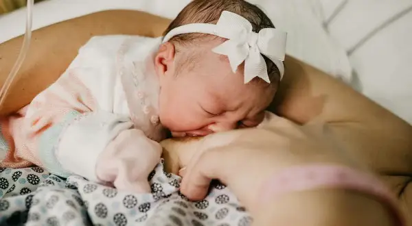 Słodki sen noworodka podczas karmienia. Maleństwo z białym memo na głowie przytula się do mamy.