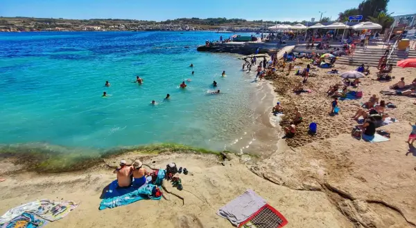 Słoneczna plaża na Malcie w październiku. Ludzie kąpią się w turkusowej wodzie i opalają na piasku. Czy warto? Zdecydowanie tak!