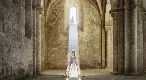 Cristina Vatielli, vestita di bianco, in piedi sotto un raggio di luce in un'antica abbazia.