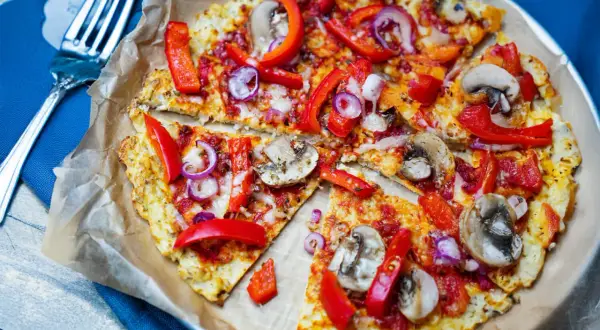 Vegane blumenkohl pizza mit Paprika, Zwiebeln und Pilzen, auf Backpapier serviert.