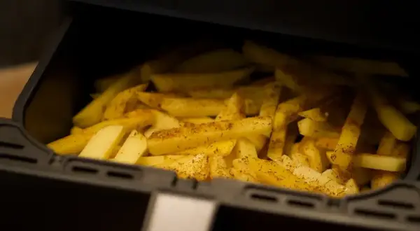 Frytki w koszu frytkownicy beztłuszczowej, przyprawione ziołami.