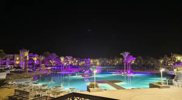 Nocny widok na basen z podświetlanymi palmami i budynkami hotelowymi. Albatros Palace Port Ghalib opinie potwierdzają jego urok.