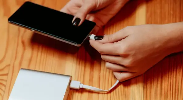 Dłonie podłączają telefon do powerbanku, by naładować baterię. Duża pojemność mah zapewni długie działanie.