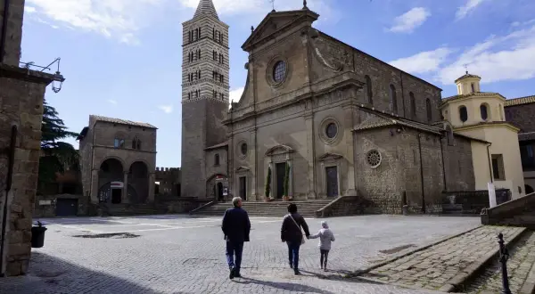 Una famiglia passeggia nella storica piazza San Lorenzo a Viterbo, ammirando la maestosa cattedrale e il suo campanile.