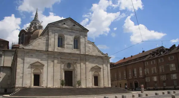 Il Duomo di Torino, con la sua imponente facciata in pietra e la cupola maestosa, si staglia sotto un cielo azzurro punteggiato di nuvole bianche.