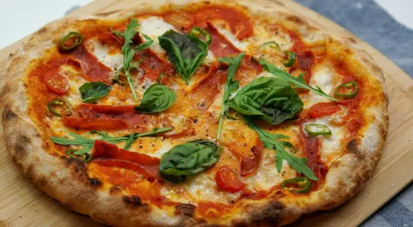 Pizza maison avec une pâte à pizza préparée la veille, garnie de tomates, mozzarella, roquette, basilic, piments et salami.
