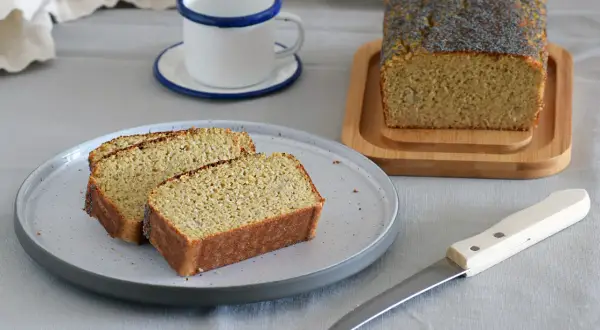 Rebanadas de bizcocho sin azucar con semillas de amapola, servidas en un plato gris junto a una taza y un cuchillo.