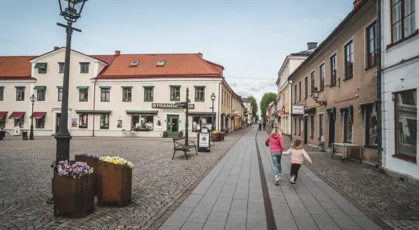 Två flickor springer glatt längs en kullerstensgata i Vadstena. Besök Vadstena för en charmig upplevelse.