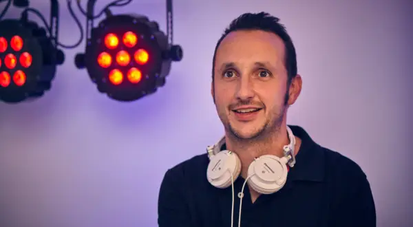 DJ mit Kopfhörern bereit für die Party in Bergisch Gladbach. Scheinwerfer leuchten im Hintergrund.