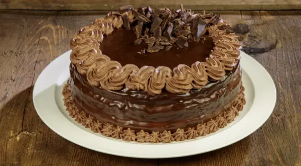 Torta compleanno cioccolato e panna, ricoperta di glassa lucida e decorata con riccioli di panna e scaglie di cioccolato.