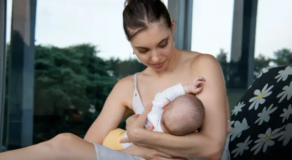 Delikatny moment karmienia piersią. Mama z miłością patrzy na swoje dziecko, które pije mleko z piersi.