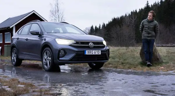 Grå VW Taigo står på en isig väg nära en röd stuga. En man står lutad mot en sten i bakgrunden.