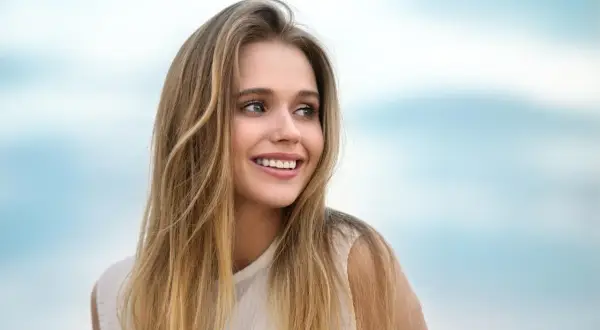 Lachendes junges Mädchen mit langen, welligen Haaren, die blonde Highlights auf dunkelblond zeigen.
