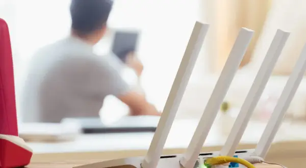 Konfiguracja routera Wi-Fi z widocznym żółtym kablem Ethernet. W tle osoba korzystająca z tabletu.