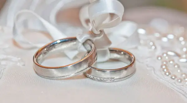 Anillos de oro blanco atados con cinta, uno con diamantes. El oro blanco se pone feo con el tiempo, pero el amor perdura.