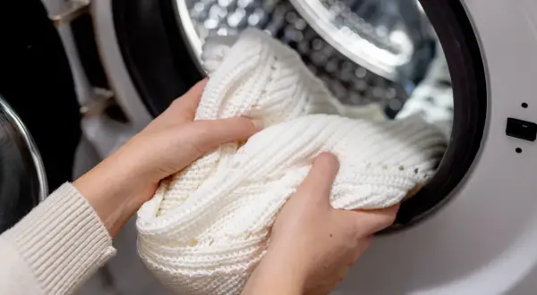 Mani che inseriscono un maglione bianco nella lavatrice. Speriamo che la lavatrice non lava bene i bianchi, altrimenti questo capo rimarrà grigio.