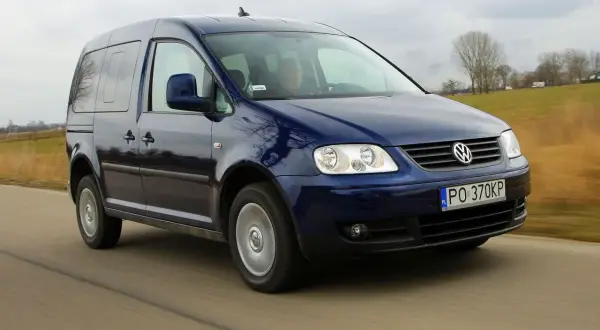 Ciemnoniebieski Volkswagen Caddy 3 w ruchu drogowym, z widocznym kierowcą.