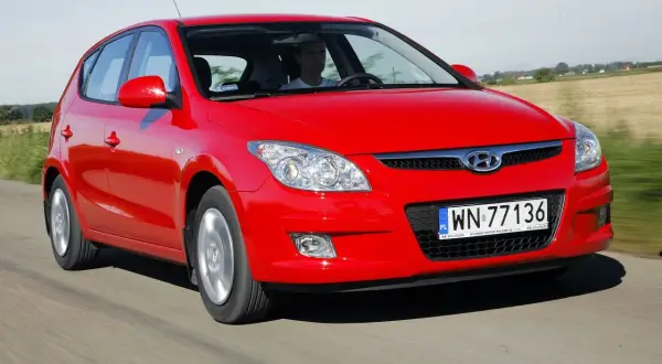 Czerwony Hyundai i30 1.6 CRDi jedzie po drodze wśród pól.