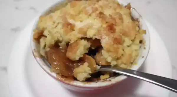 Un delizioso crumble di mele appena sfornato, con la crosta dorata e il ripieno succoso. Una forchetta è immersa nel dolce.