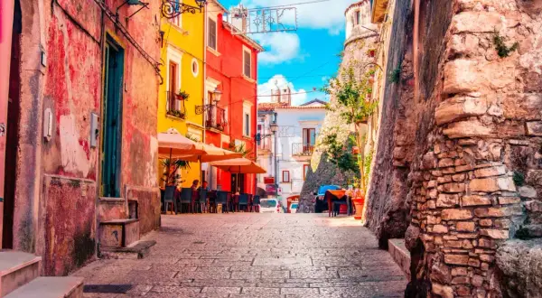 Vico del Gargano, Vicolo del Bacio: un vicolo pittoresco con case colorate, tavolini all'aperto e un'antica muraglia di pietra.