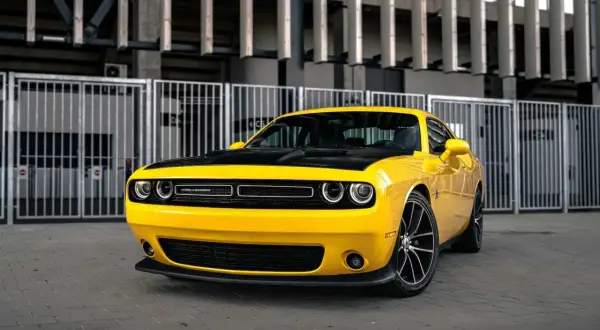 Żółty Dodge Challenger 5.7 Hemi z czarną maską, zaparkowany przed nowoczesnym budynkiem.