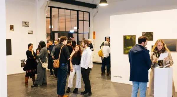 Besucher auf einer **Foto Messe Hamburg** diskutieren Kunstwerke in einer hellen Galerie.