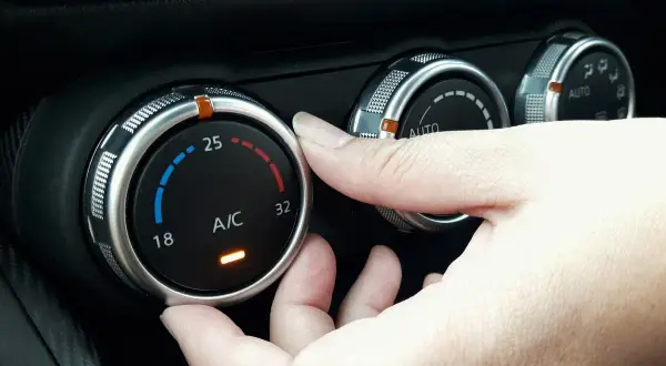 Dłoń reguluje pokrętłem temperaturę klimatyzacji w samochodzie, ustawiając ją na 25 stopni.