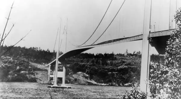 Die Tacoma-Brücke überspannt ein Gewässer, umgeben von bewaldeten Hügeln.