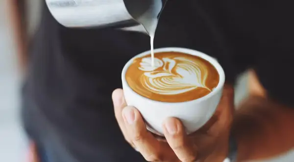 Un barista crea un disegno a latte art su un cappuccino. Latte versato nel caffè per un cappuccino prima latte o caffè perfetto.