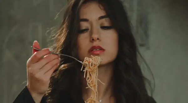 Włoska uroda w pełnej krasie. Kobieta z ciemnymi włosami i czerwoną szminką na ustach je spaghetti.