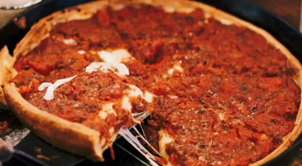 Ein Stück einer tiefen Chicago Style Pizza mit geschmolzenem Käse wird herausgehoben.