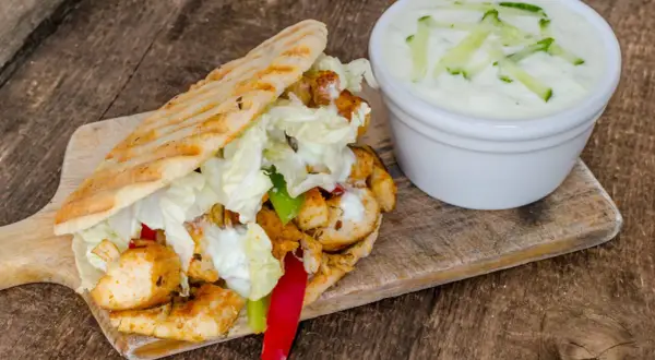 Gyros z kurczakiem, warzywami i sosem tzatziki na desce drewnianej.