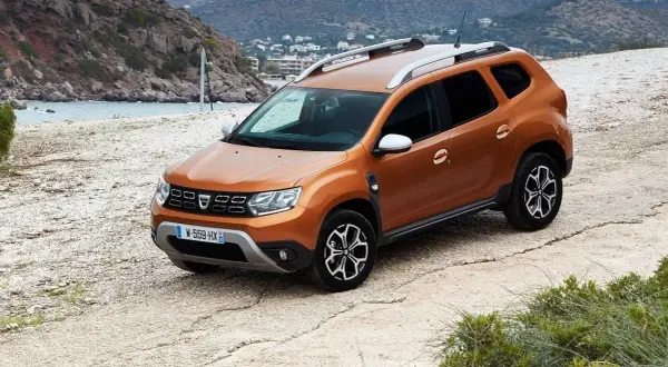 Pomarańczowy Dacia Duster na drodze szutrowej. Wiele osób szuka dacia duster opinie forum, by dowiedzieć się więcej o tym modelu.