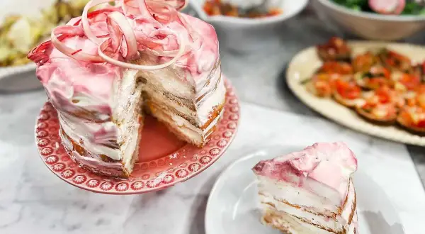 En vacker rabarberkompott tårta med rosa glasyr och dekorationer. En bit är upplagd på en tallrik.