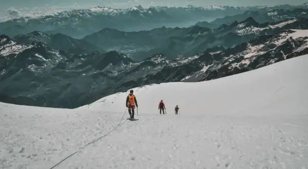 Trois alpinistes progressent sur un glacier enneigé, le Mont Rose en toile de fond. L'ascension est spectaculaire.