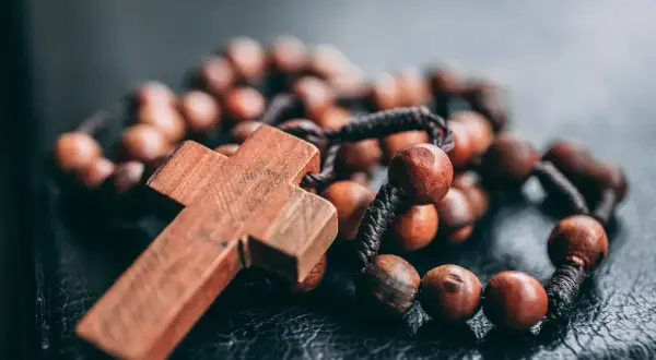 Drewniany różaniec na czarnej powierzchni. Różaniec to symbol wiary, ale czym się różni katolik od chrześcijanina?