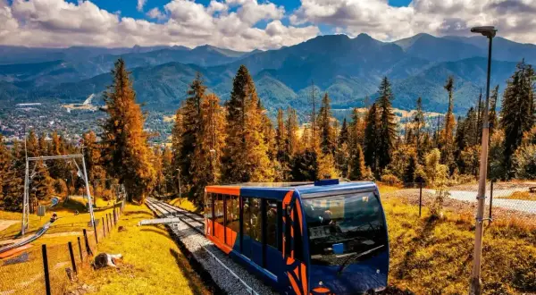 Kolejka na Gubałówkę w jesiennej odsłonie. Widok na góry i lasy, wagonik na torach.