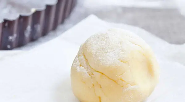 Une boule de pâte sucrée amande, saupoudrée de sucre glace, prête à être utilisée dans un moule à tarte.