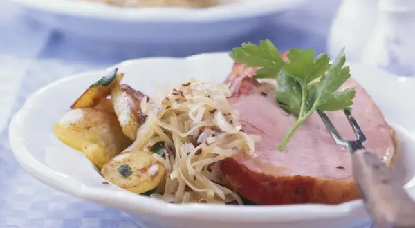 Herzhaftes Fleisch zu bayrisch Kraut mit Bratkartoffeln, garniert mit Petersilie. Ein Klassiker der bayerischen Küche.
