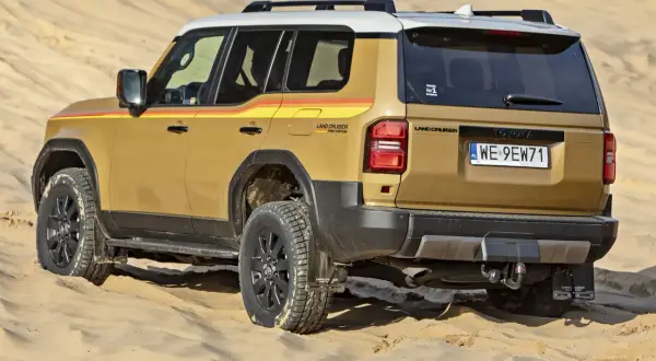 Złoty Land Cruiser z kolorowymi pasami na boku, gotowy na przygodę w piaskach pustyni, niczym potężna sequoia w krajobrazie.