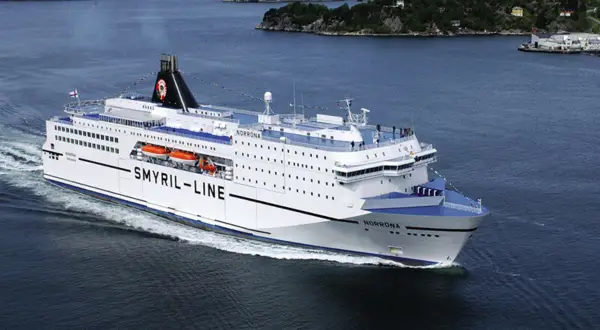 Norröna, prom Smyril Line, płynie przez spokojne wody. W tle widać zielone wzgórza i zabudowania. Idealny widok na podróż na Wyspy Owcze.