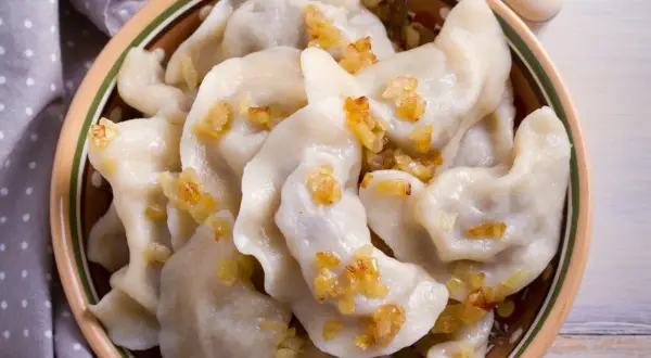 Pierogi chłopskie z podsmażoną cebulką w glinianej misce.