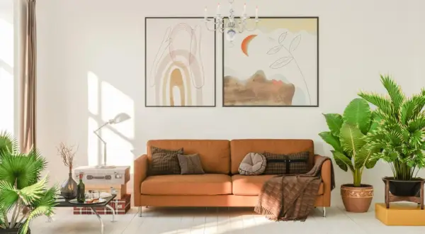 Ein gemütliches Wohnzimmer mit einem orangefarbenen Sofa, das mit Kissen und einer Decke dekoriert ist. Die Sofa-Farbe passt gut zu den Pflanzen und Bildern.